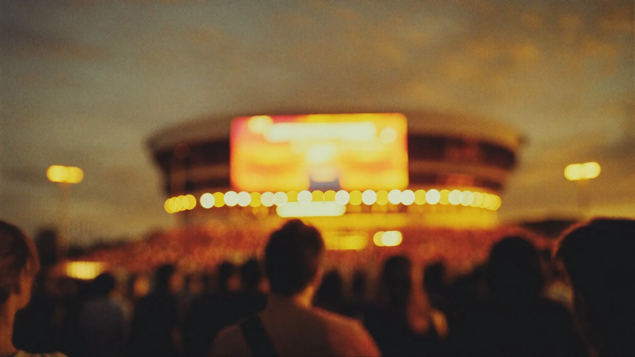 Warm defocused lights of a glowing arena above an evening crowd