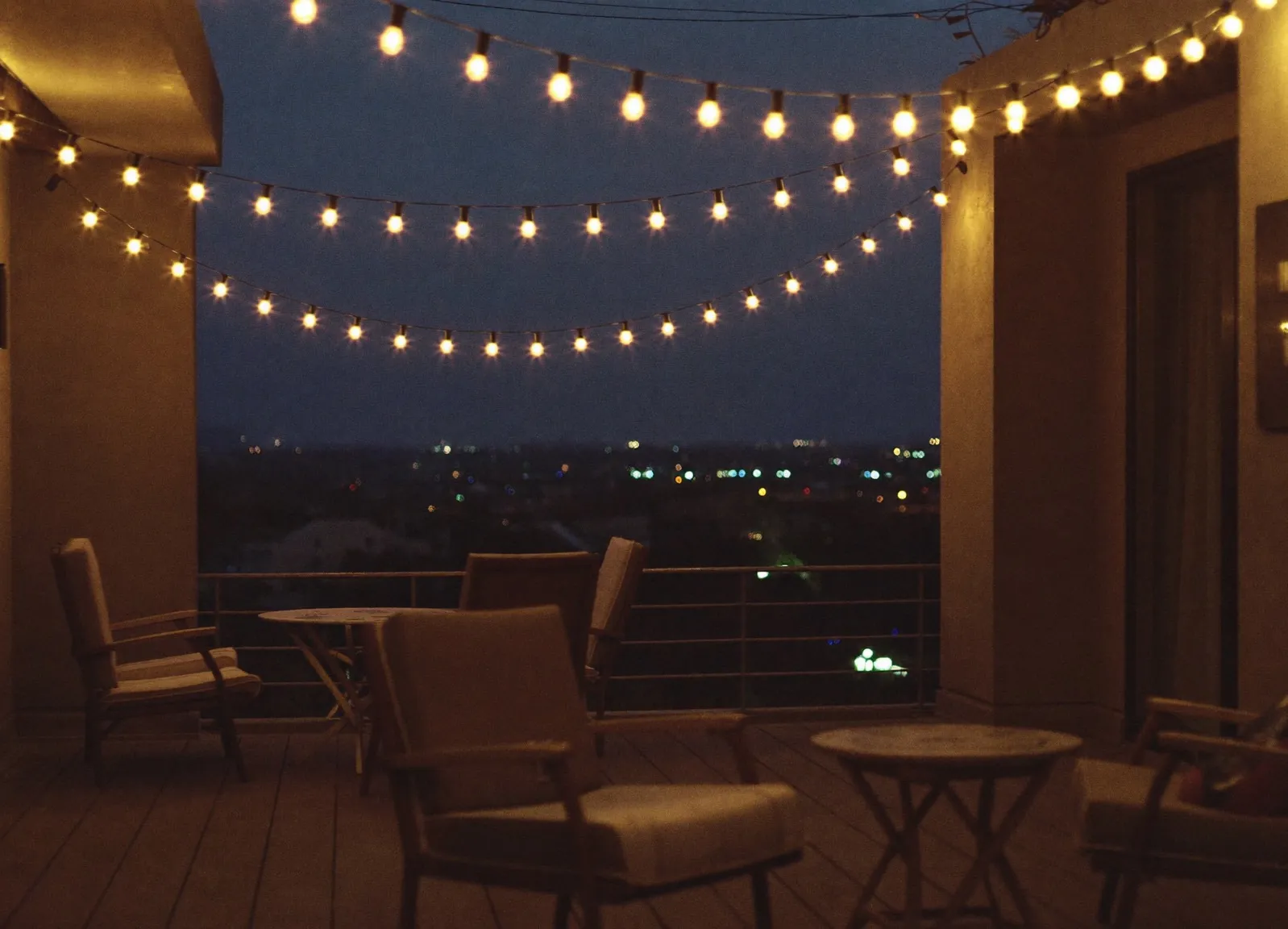 String lights over a rooftop patio at dusk with city lights beyond